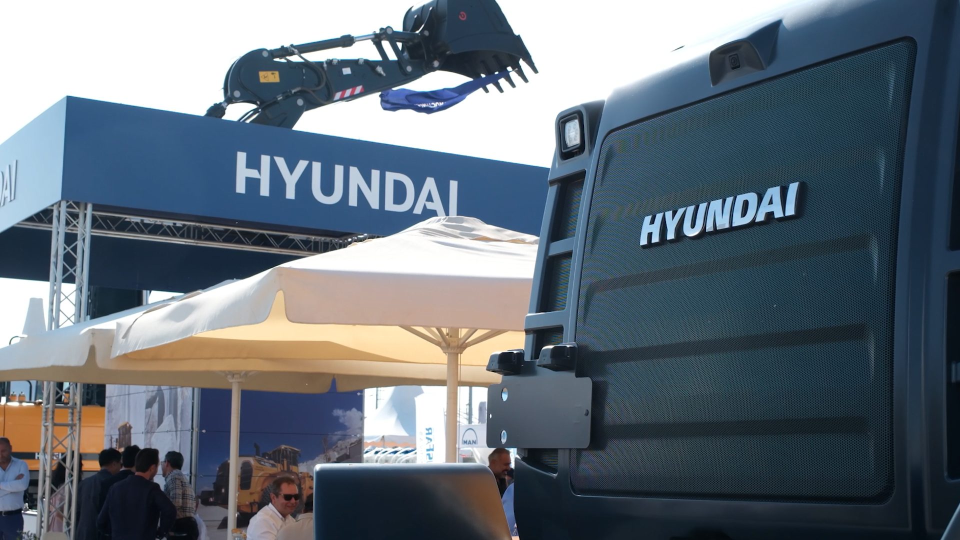 Hyundai exhibition booth with an excavator, heavy equipment, and attendees.
