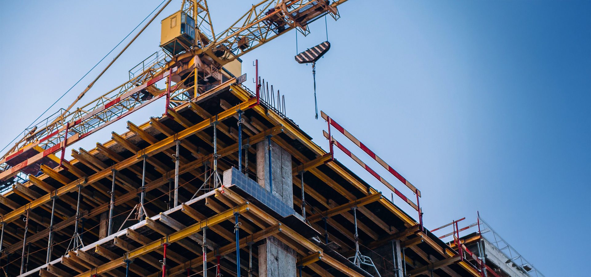 Construction site with a yellow crane and building frame against a clear blue sky.