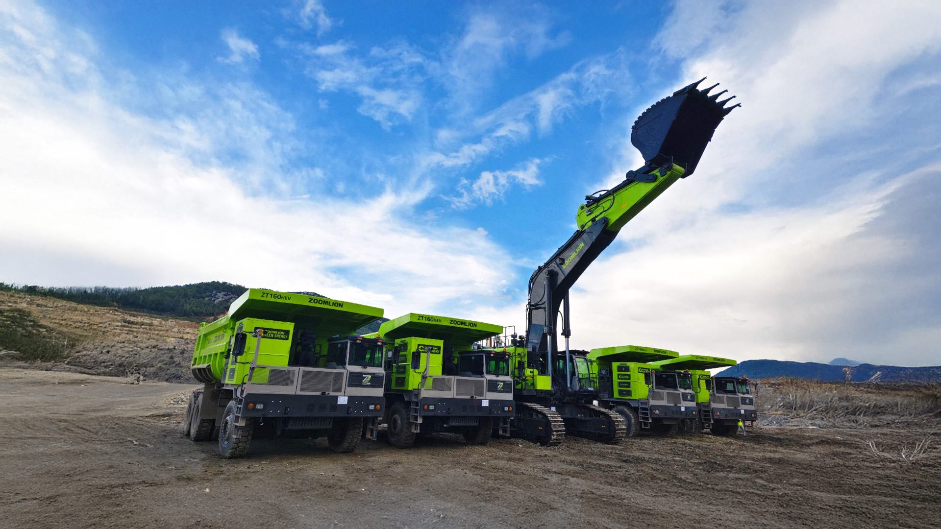 Several lime green mining trucks and a large excavator parked on dirt under a cloudy sky.