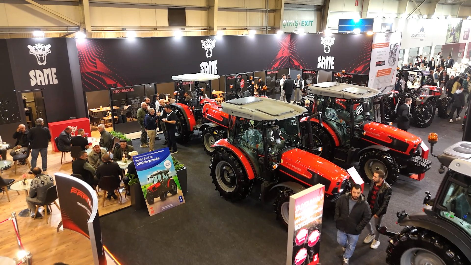 Aerial view of a tractor exhibition hall with red SAME tractors and people.