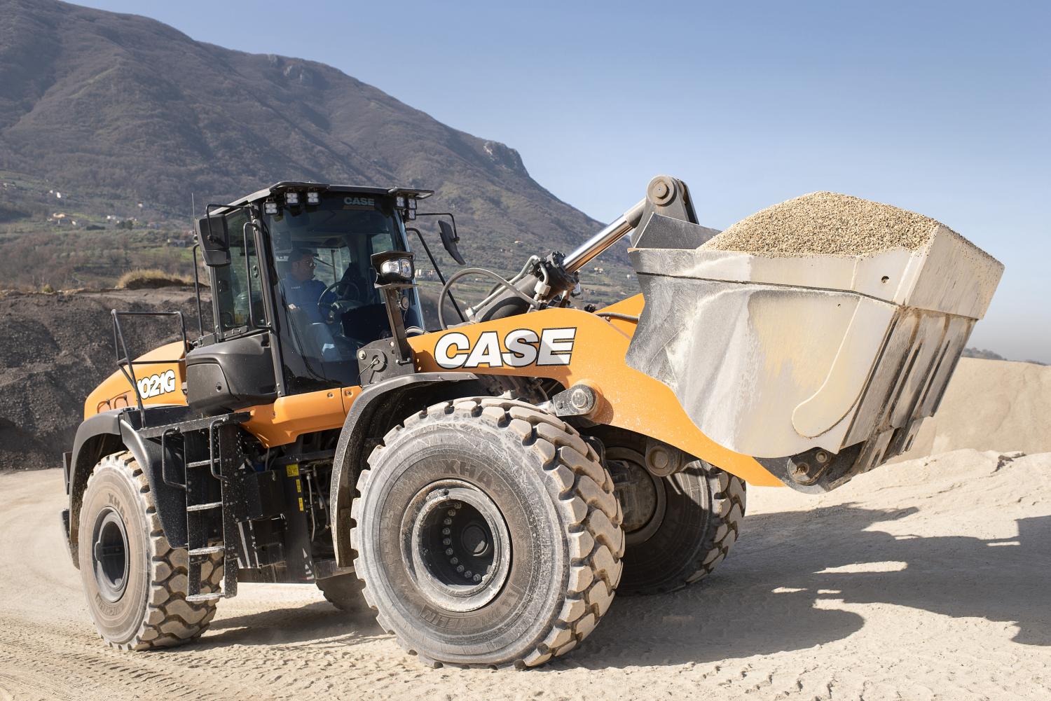 Orange Case wheel loader with a full bucket of gravel at a quarry with mountains.