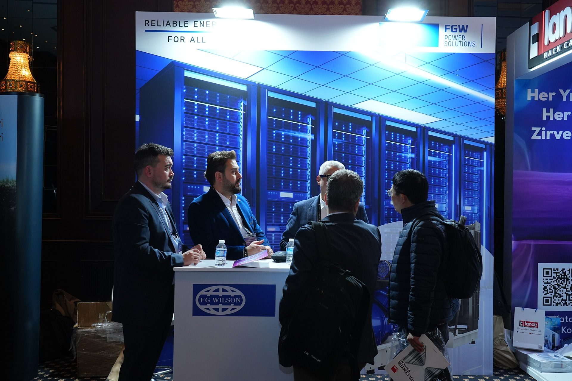 Attendees at an FG Wilson booth, featuring a data center backdrop and "RELIABLE ENERGY FOR ALL".