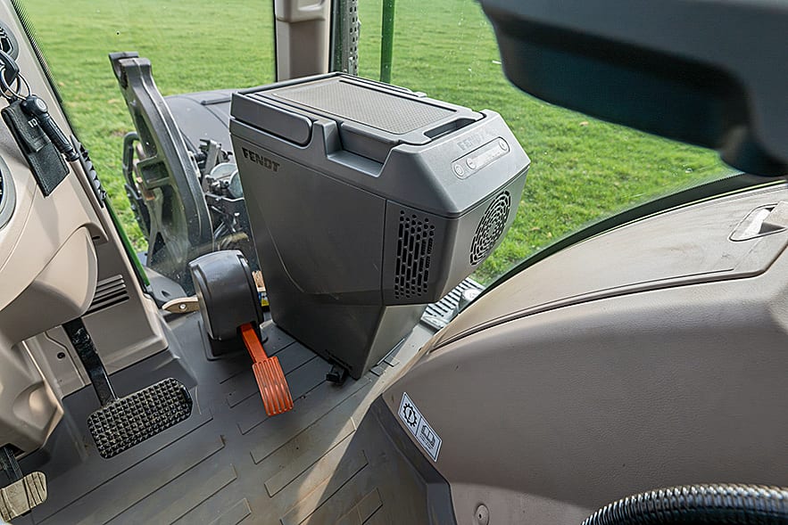 Fendt tractor interior: pedals, Fendt cooler, and a green field visible through the window.