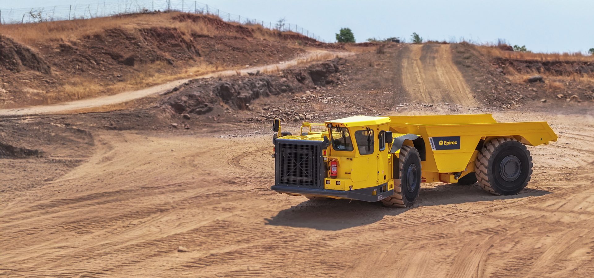 Yellow Epiroc mining truck on a dirt road in a dry, open-pit mine.