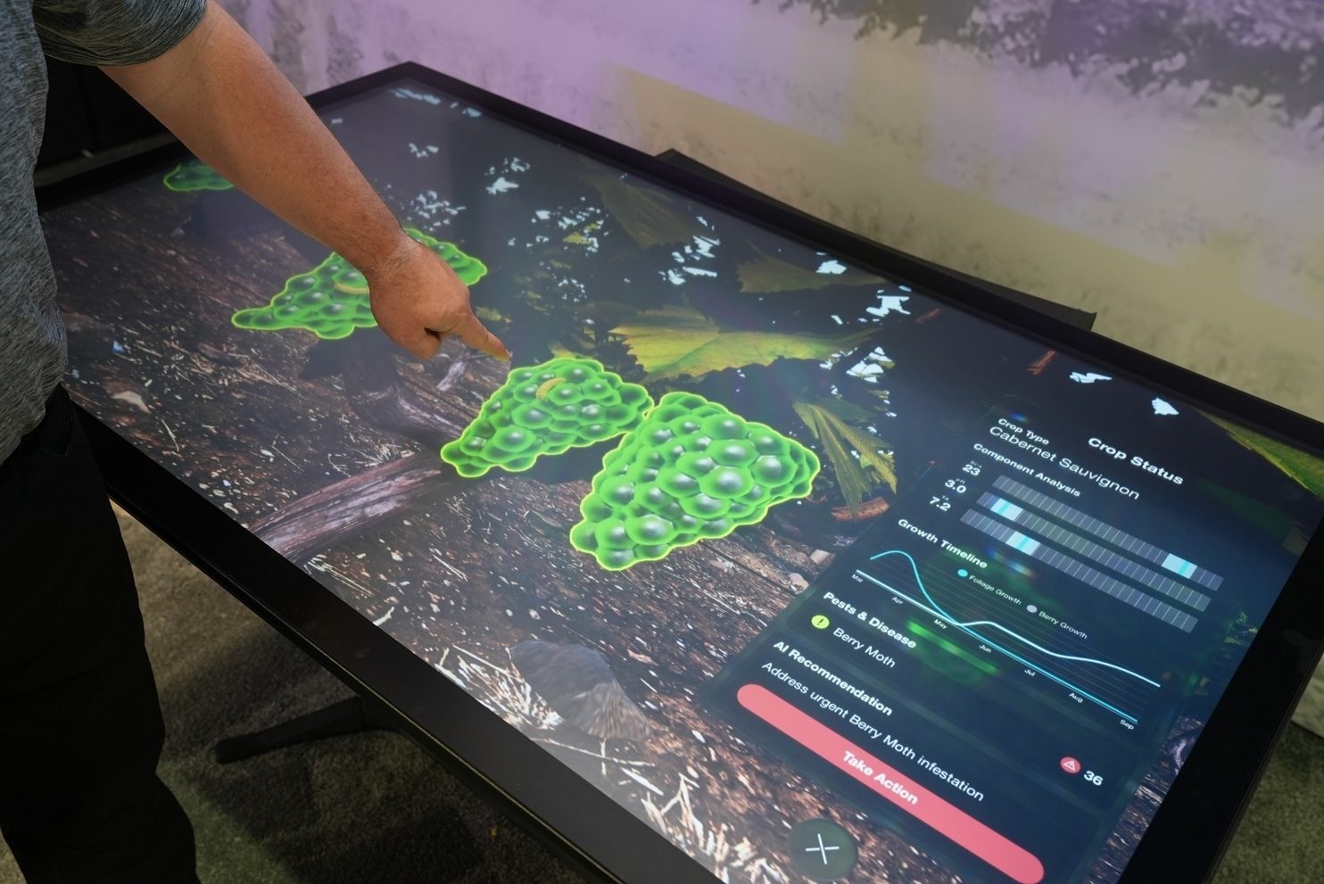 Hand on touchscreen showing vineyard data, grape clusters, and AI pest recommendation.