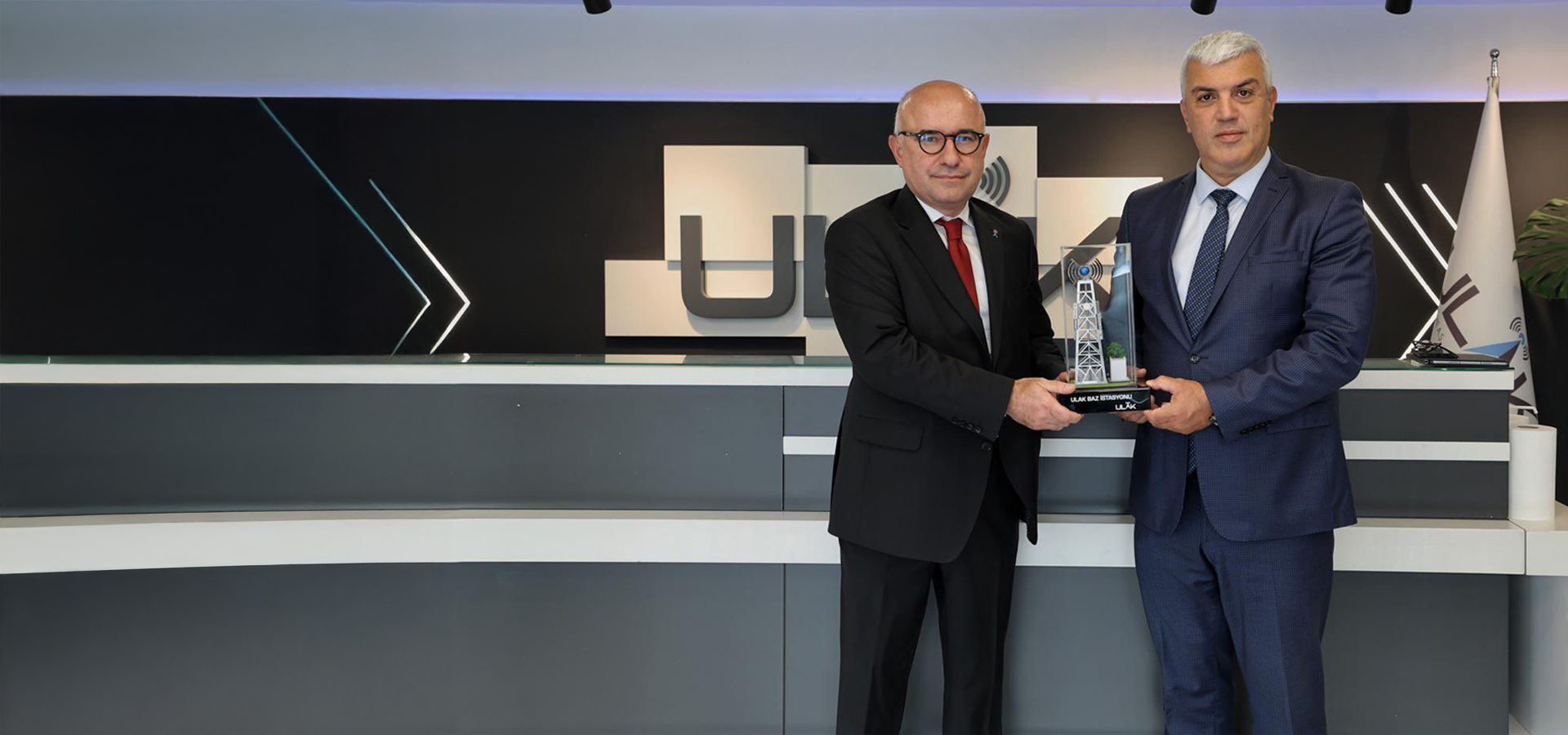 Two men in suits holding a trophy resembling a communication tower.