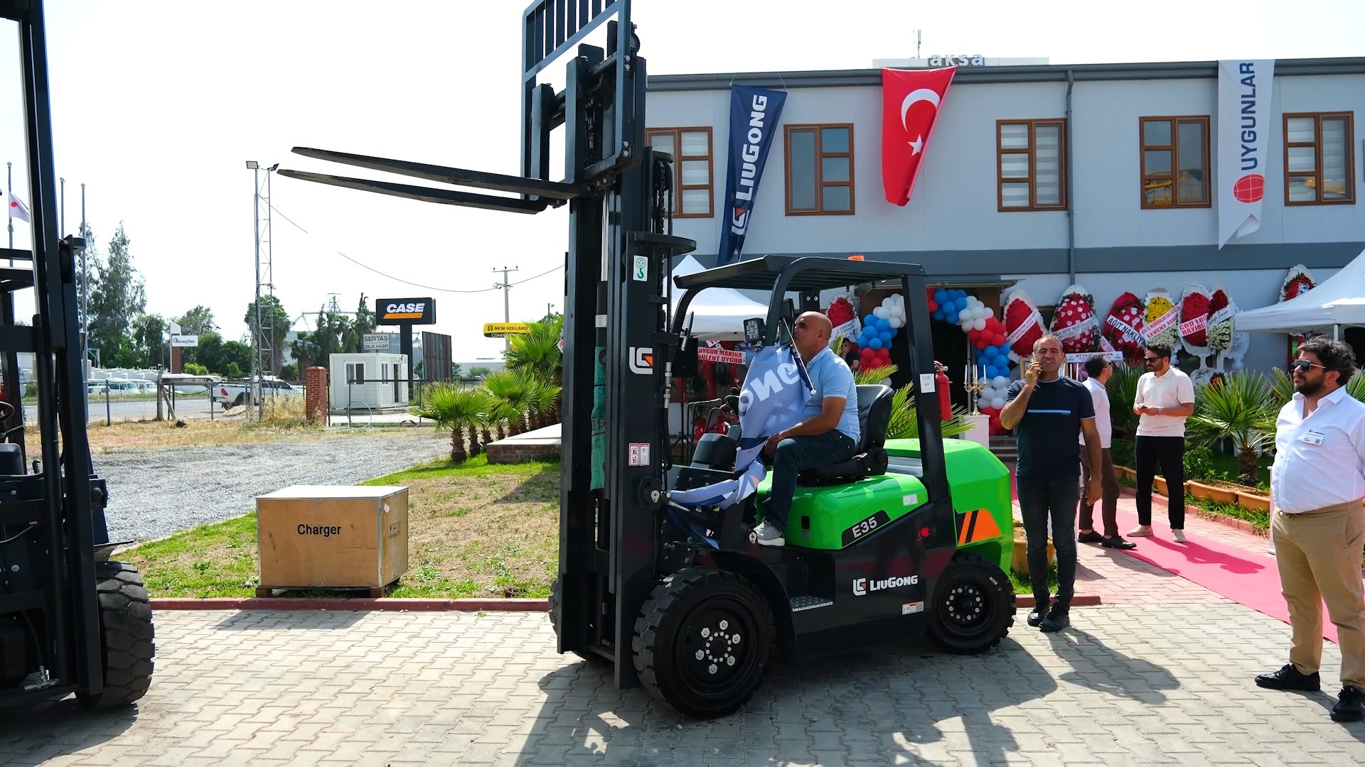 Man on green Liugong E35 forklift at an outdoor event with people and a 'Charger' box.