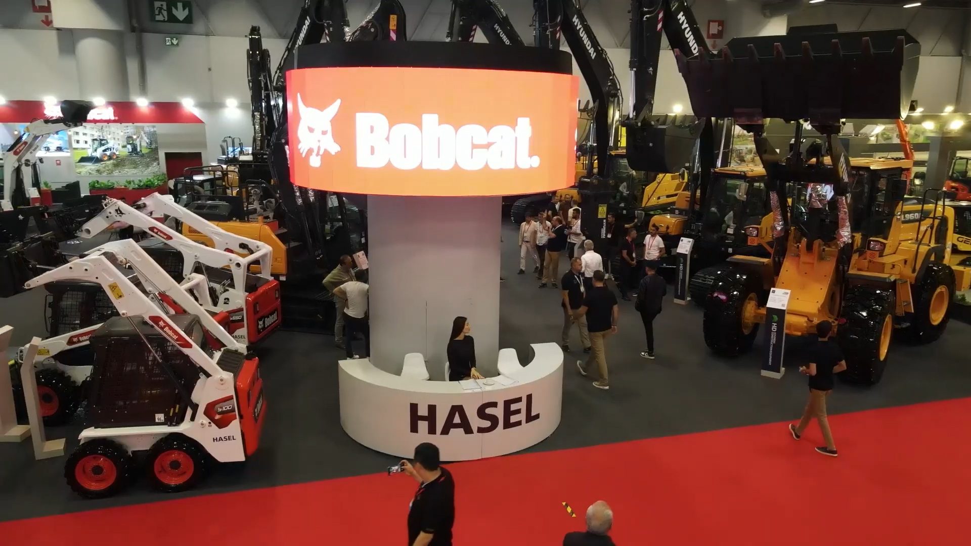 Bobcat trade show exhibit with heavy construction machinery, including skid-steer loaders, and attendees.