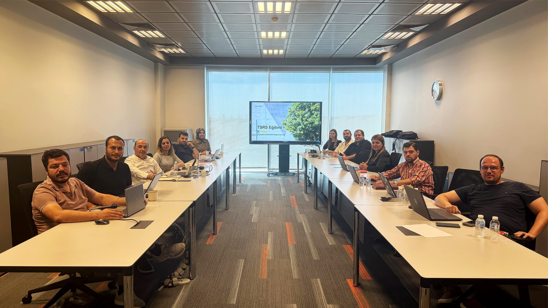 People in a modern meeting room attending a training session with "TSRS Eğitimi" on screen.