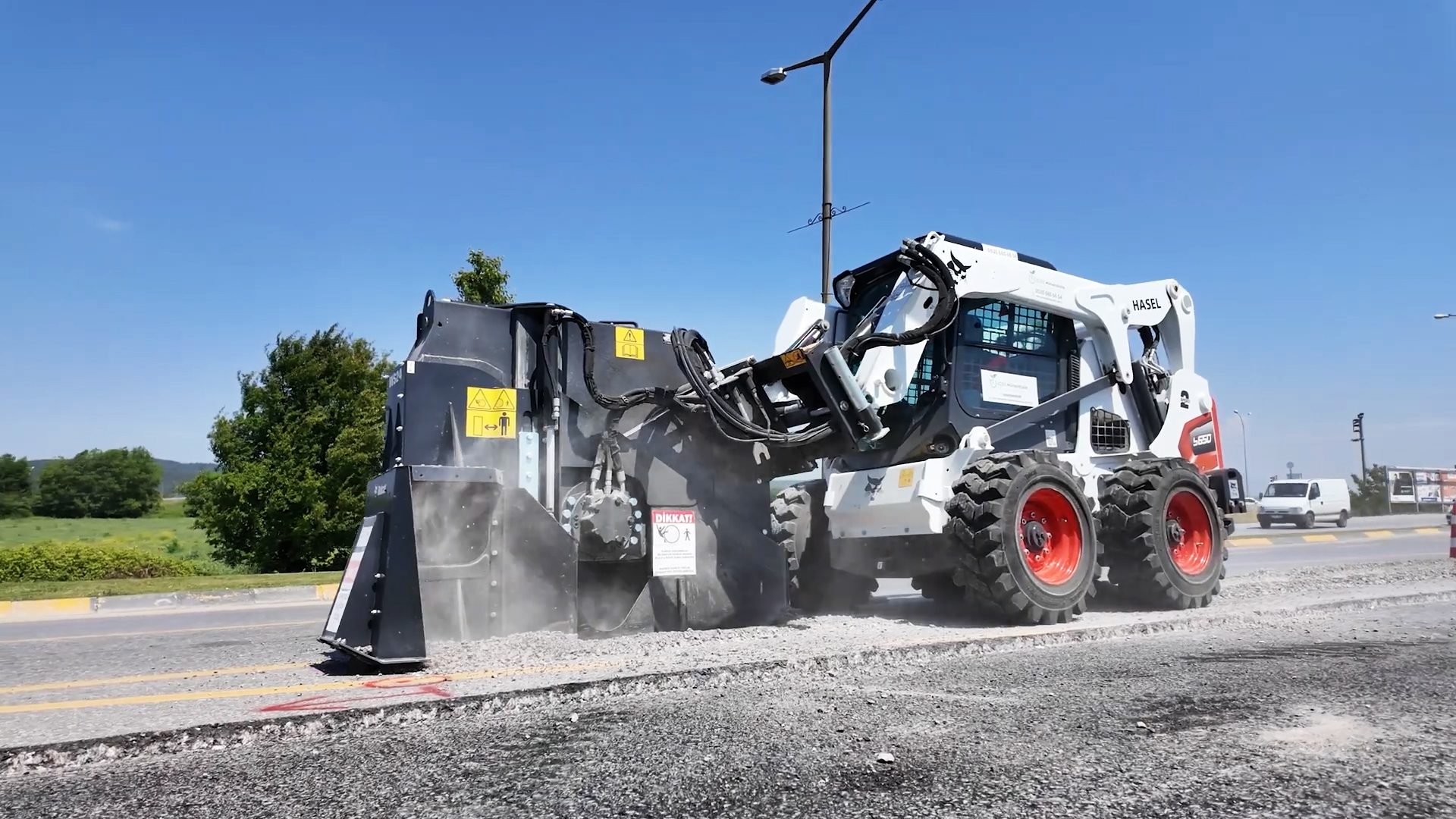 A Bobcat skid-steer loader with a milling attachment removes asphalt from a road.