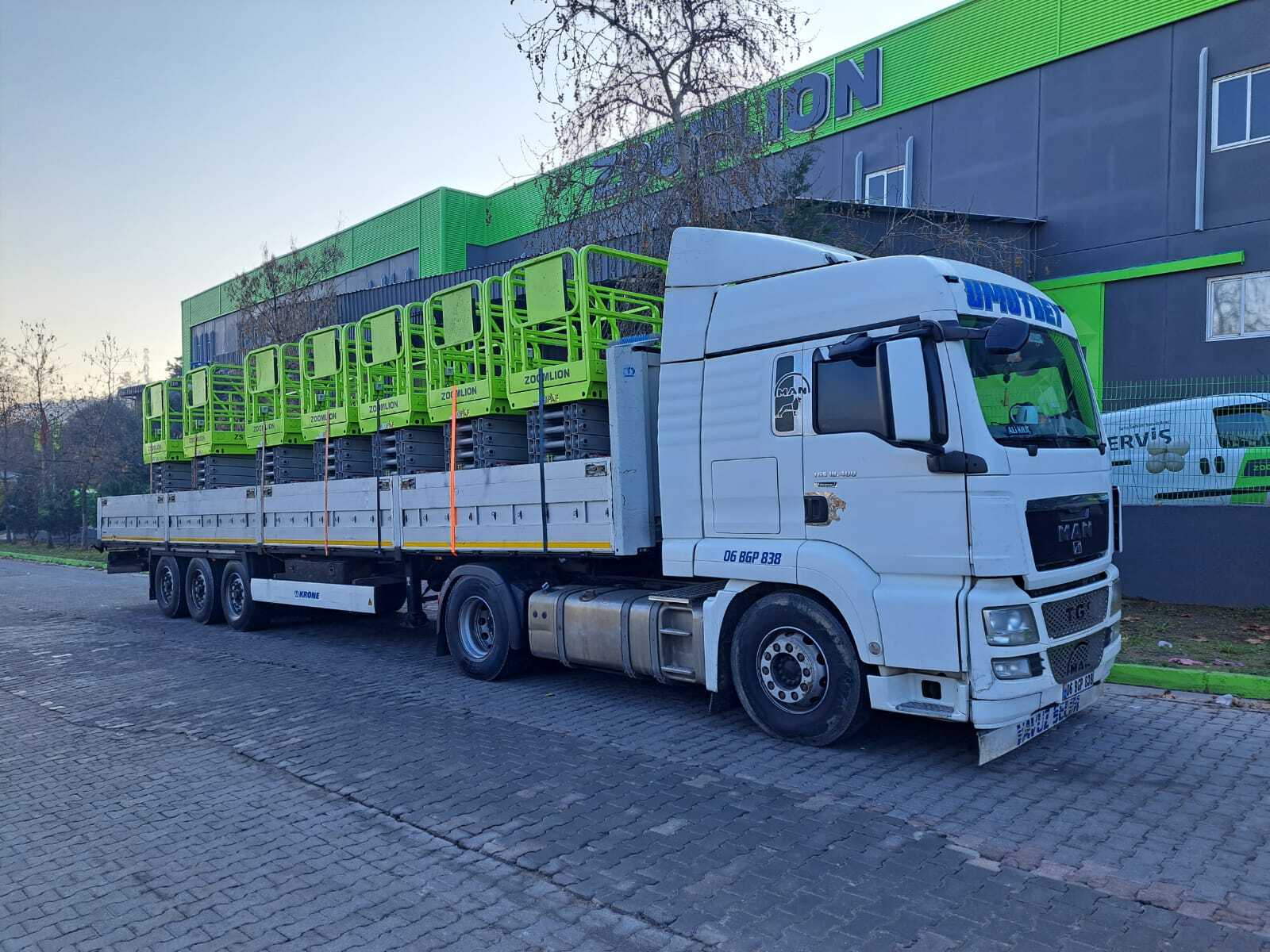 A white semi-truck (06 BGP 838) hauls bright green Zoomlion scissor lifts on a flatbed trailer.