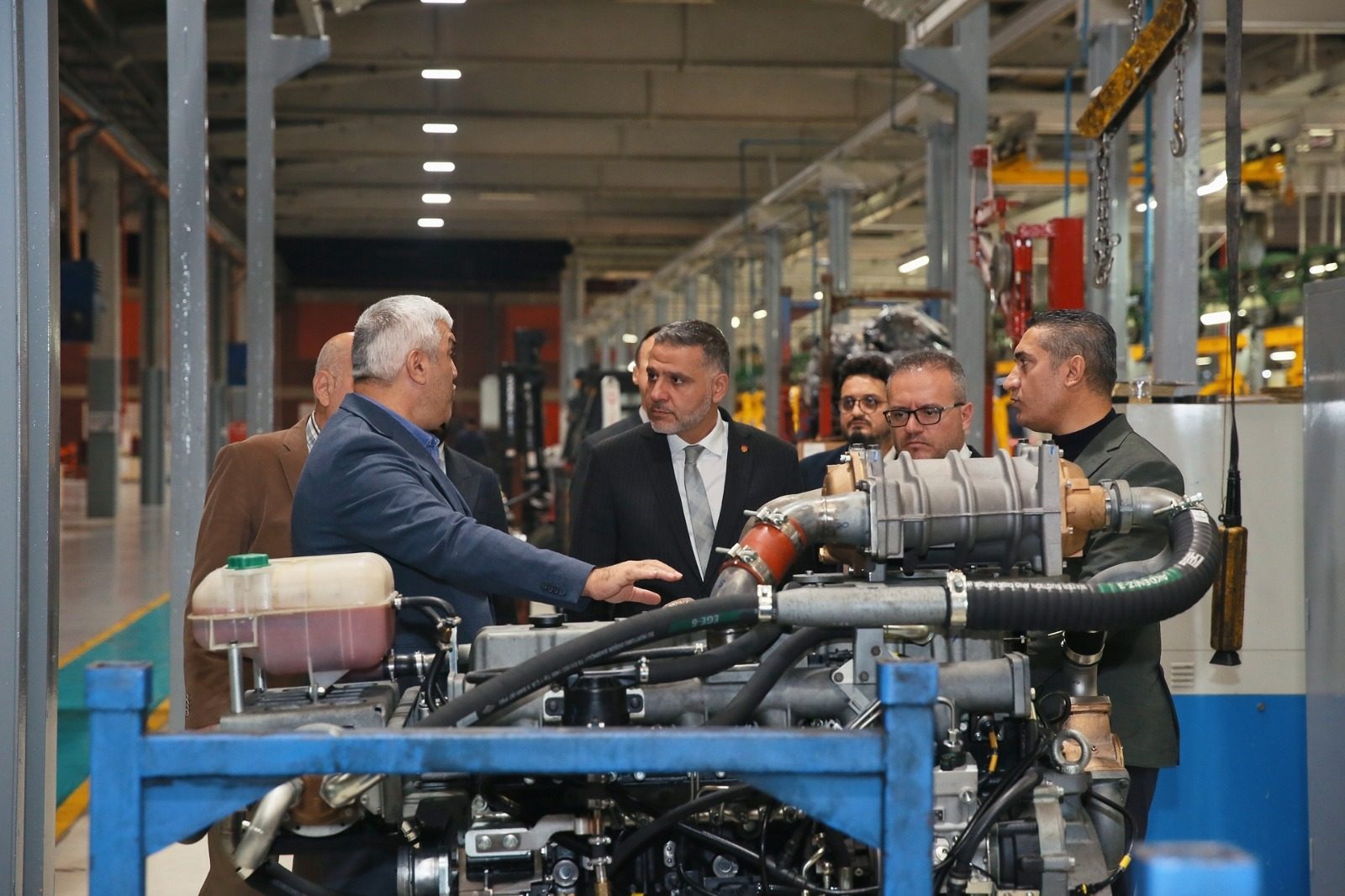 A group of men in a factory inspecting an engine, with one man pointing.