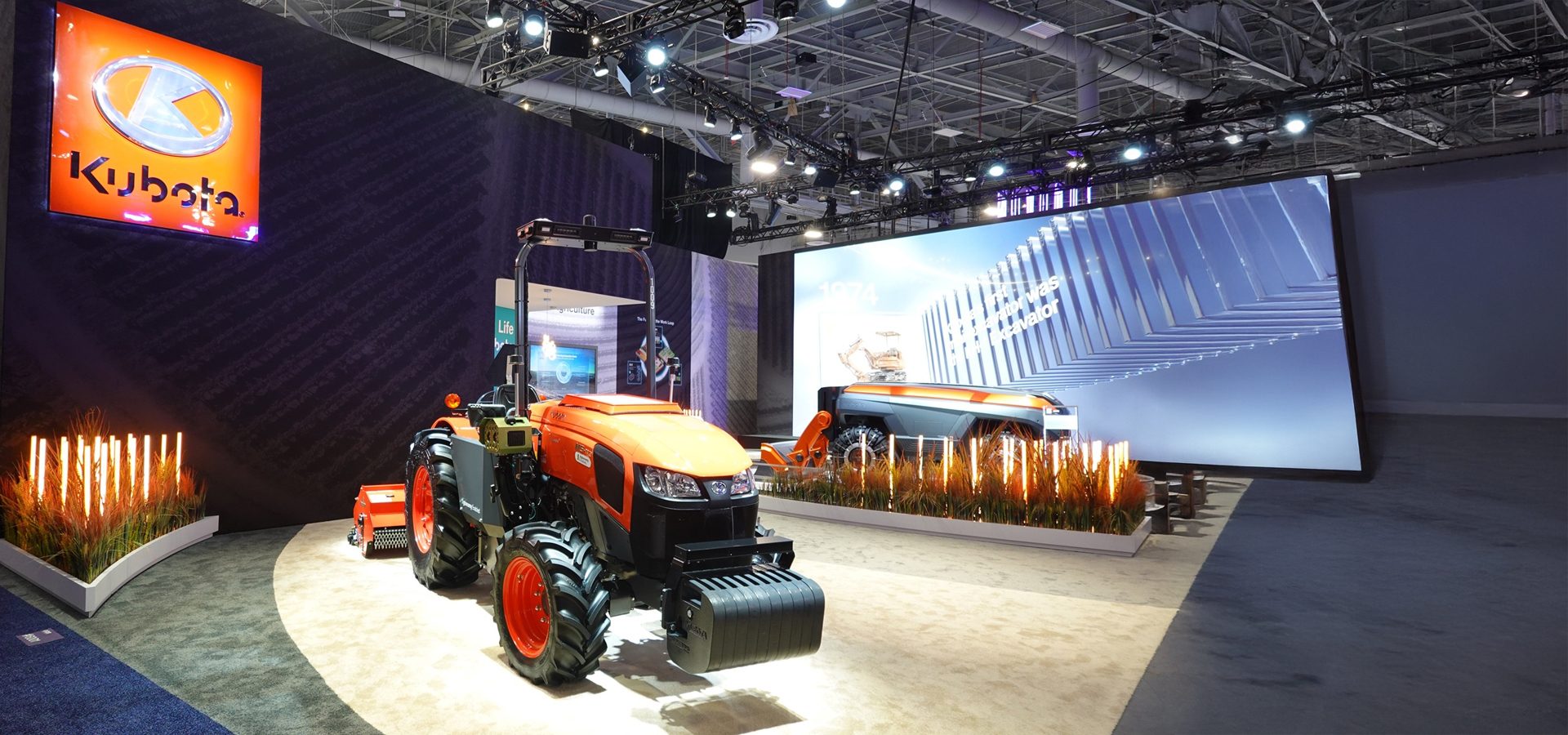 Kubota exhibition booth with orange tractor, large screen, and logo.