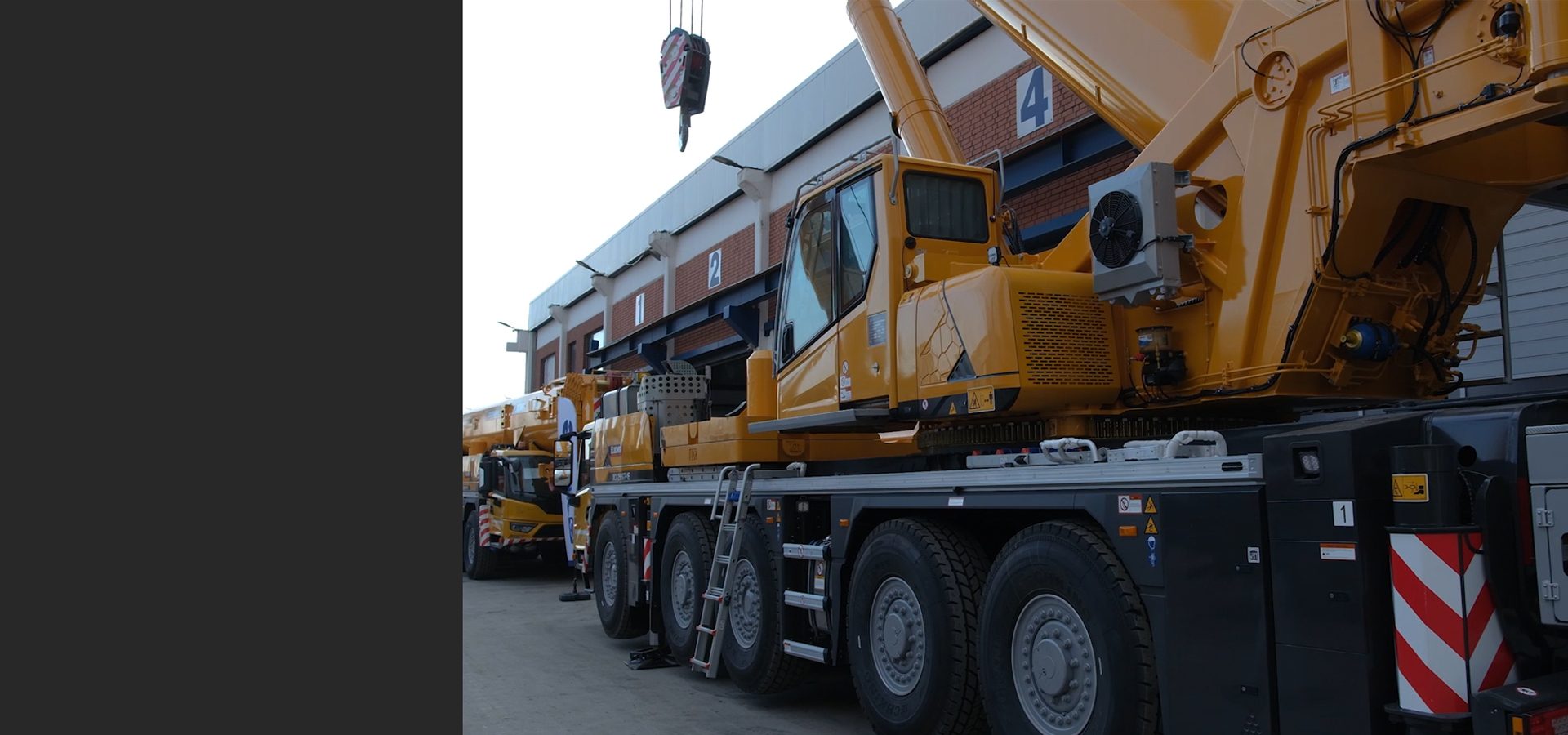 Large yellow mobile cranes parked outside a building, with one crane's hook visible.