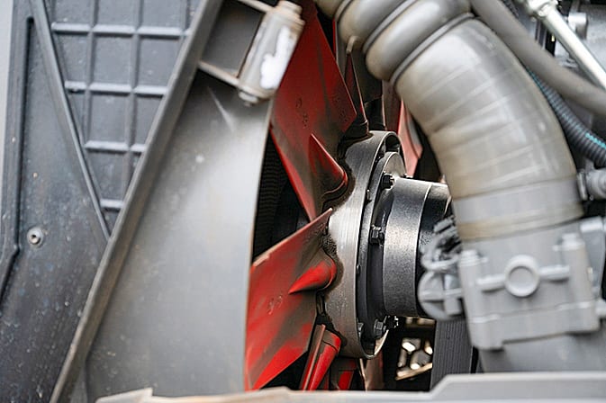 Dirty red fan blades and metallic engine components in a vehicle engine.