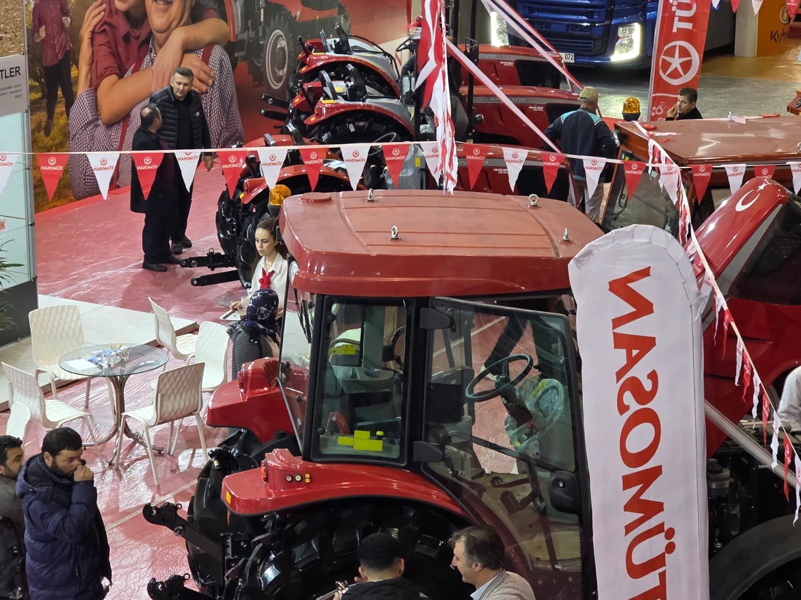 Overhead view of an indoor event featuring red tractors, people, and "MAZOMOT" branding.
