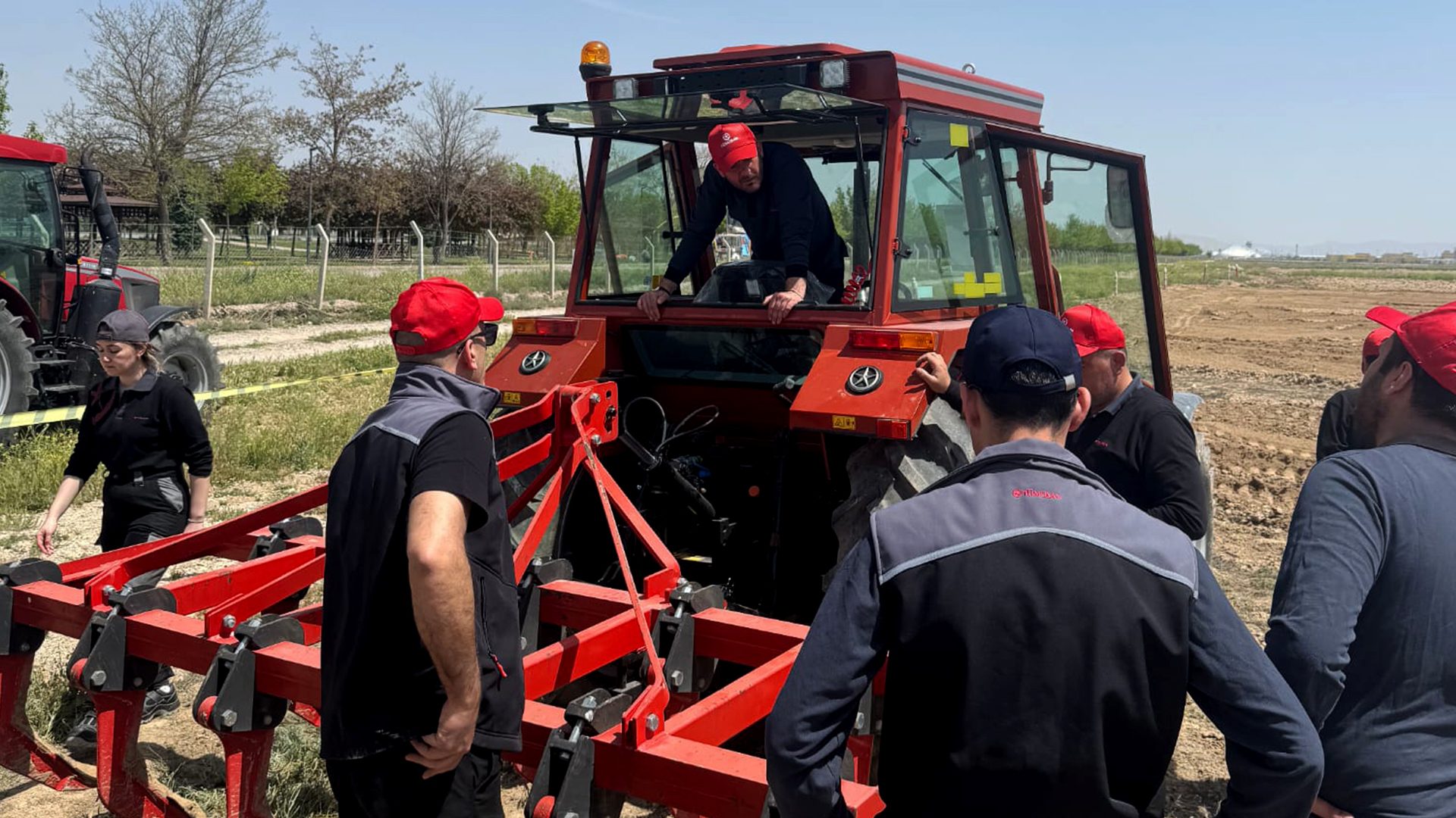 People inspect a red tractor and its agricultural implement in a field.