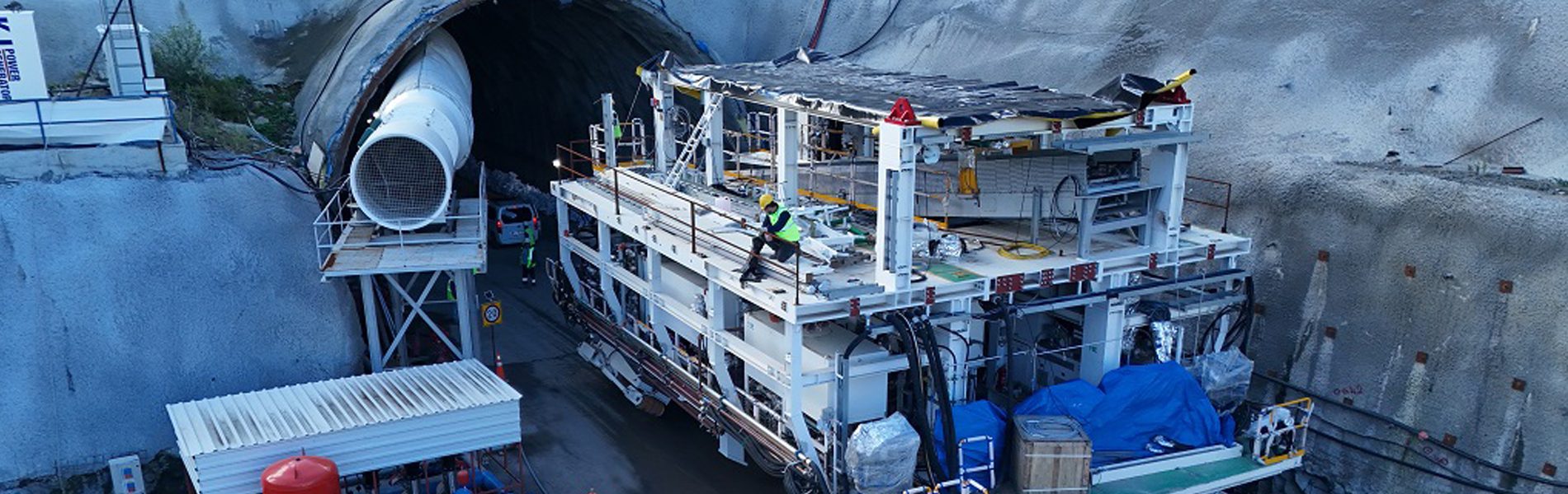 Large tunnel boring machine back-up system, ventilation, and workers at a tunnel entrance construction site.