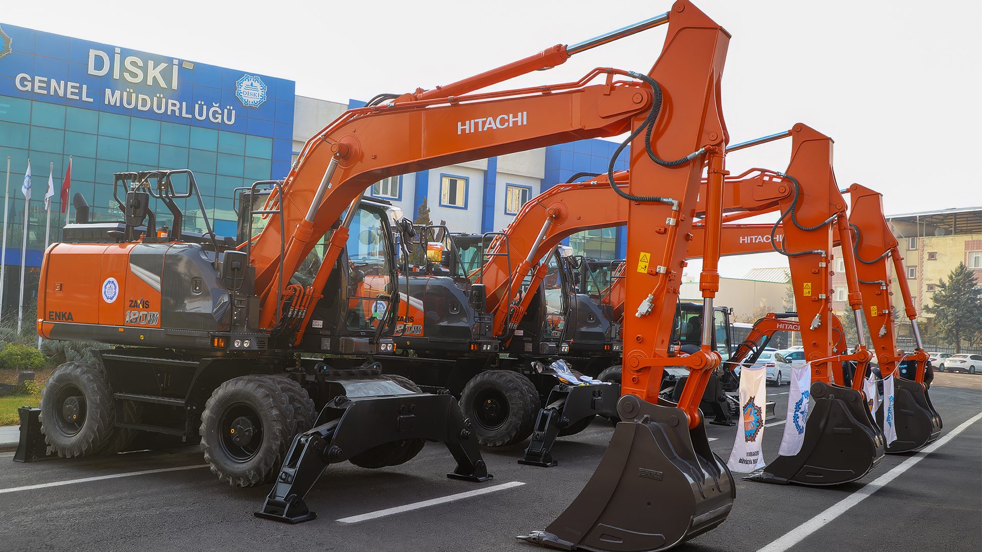 Row of orange Hitachi excavators parked in front of a building with "Diski Genel Müdürlüğü" signage.