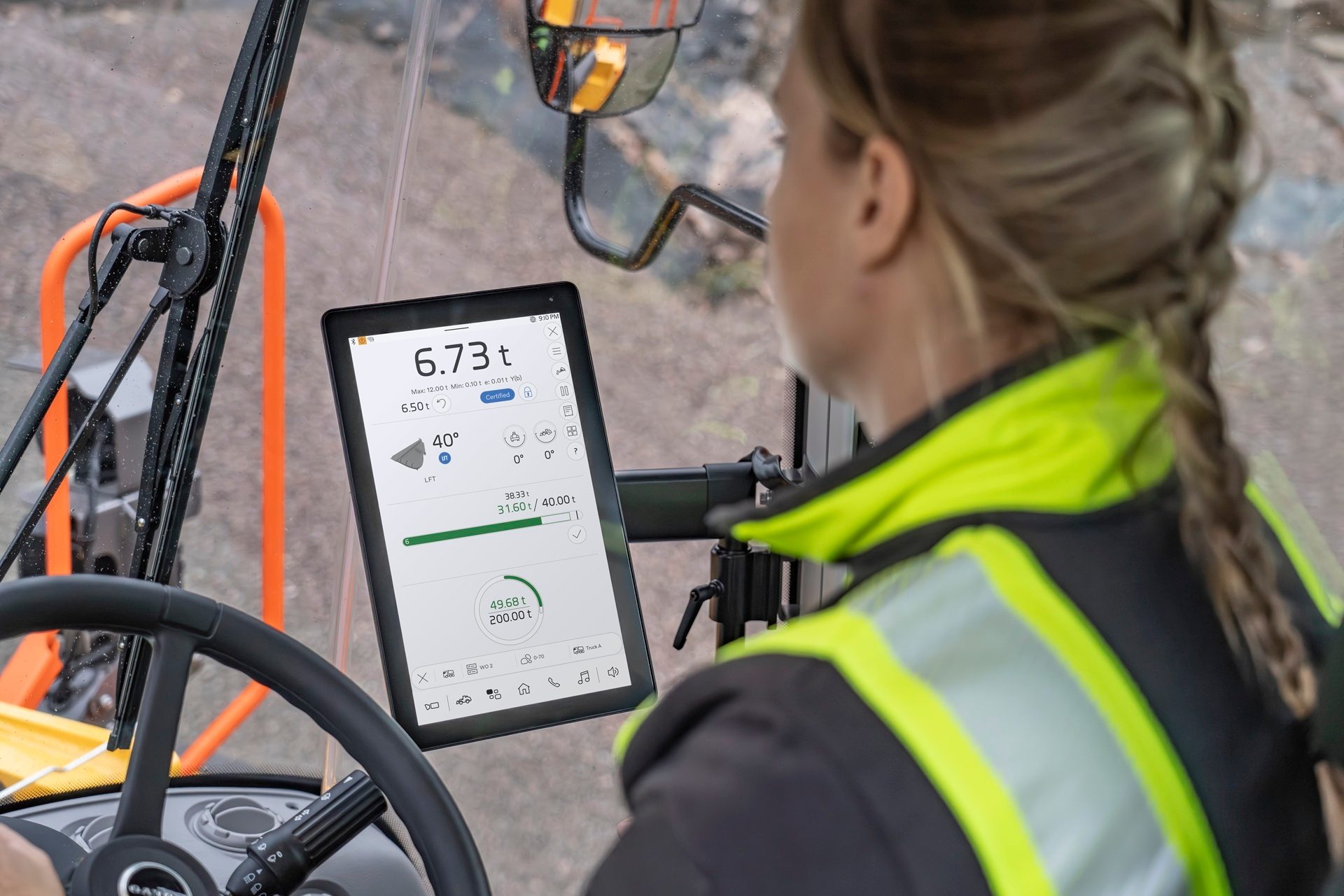 A worker in a high-vis jacket operates heavy machinery, viewing a digital display with measurements.