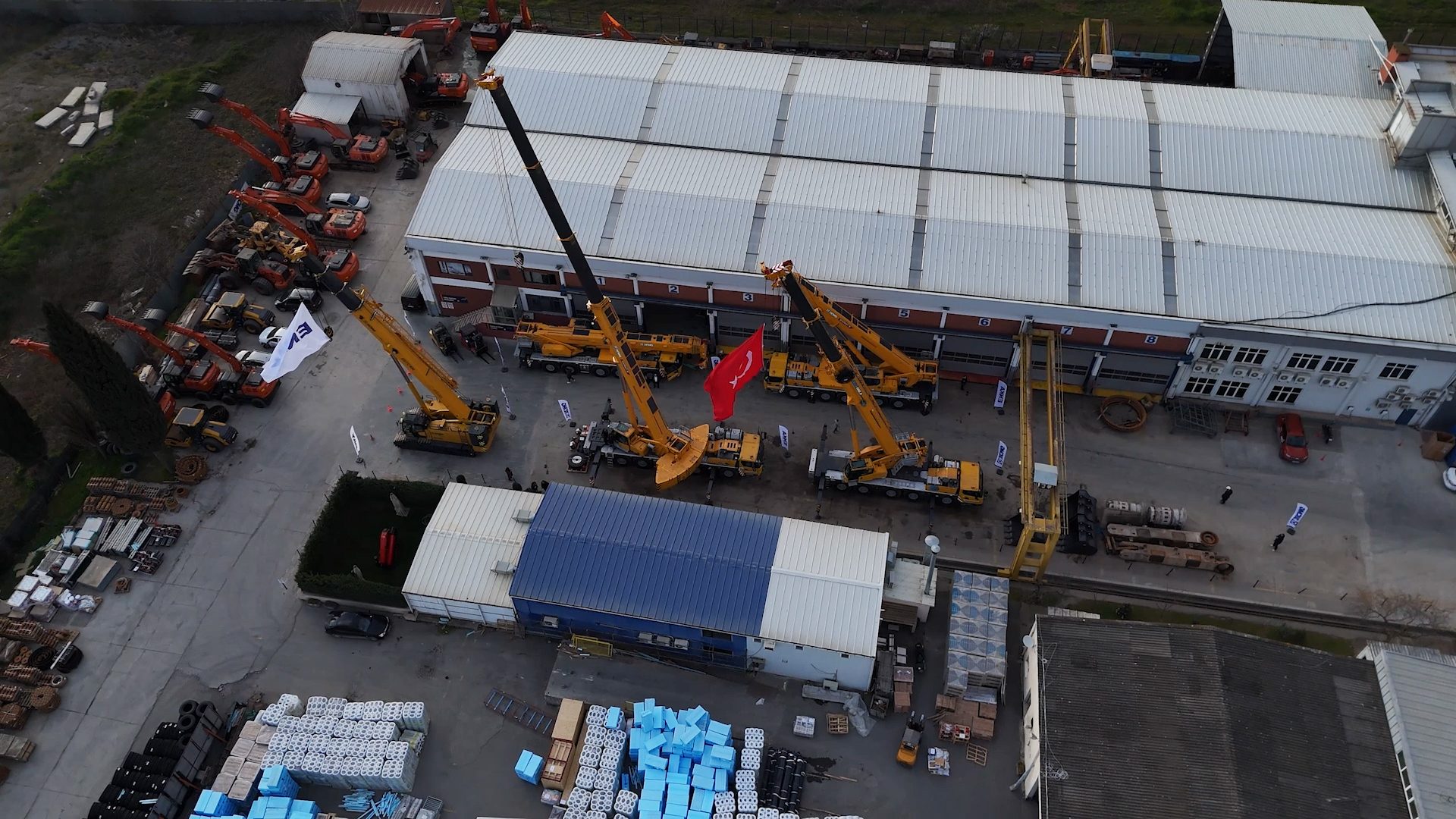 Aerial view of a facility showing numerous yellow cranes, excavators, a large building, and materials.