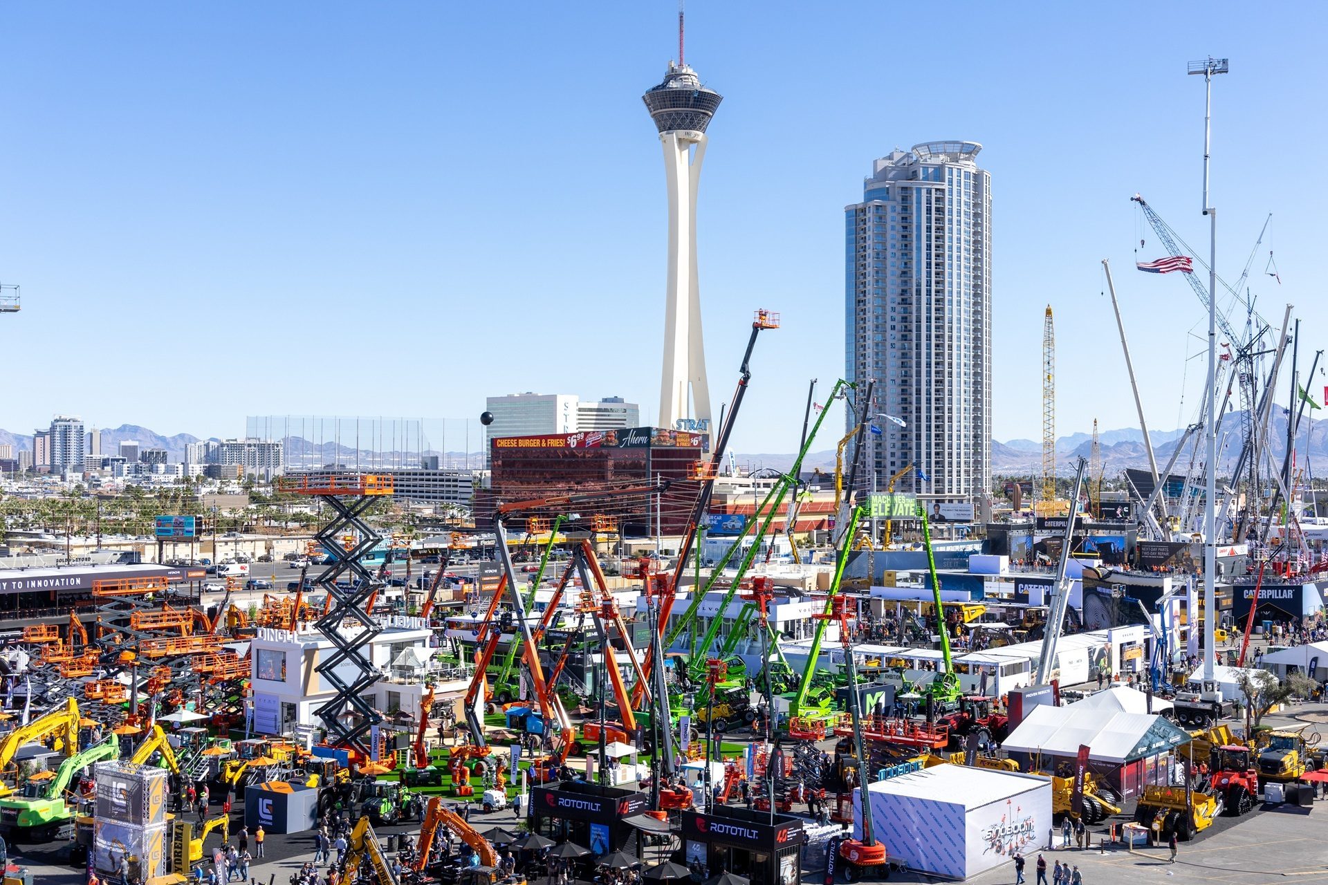 Outdoor heavy equipment exhibition with excavators, cranes, and boom lifts under the Las Vegas Stratosphere Tower.
