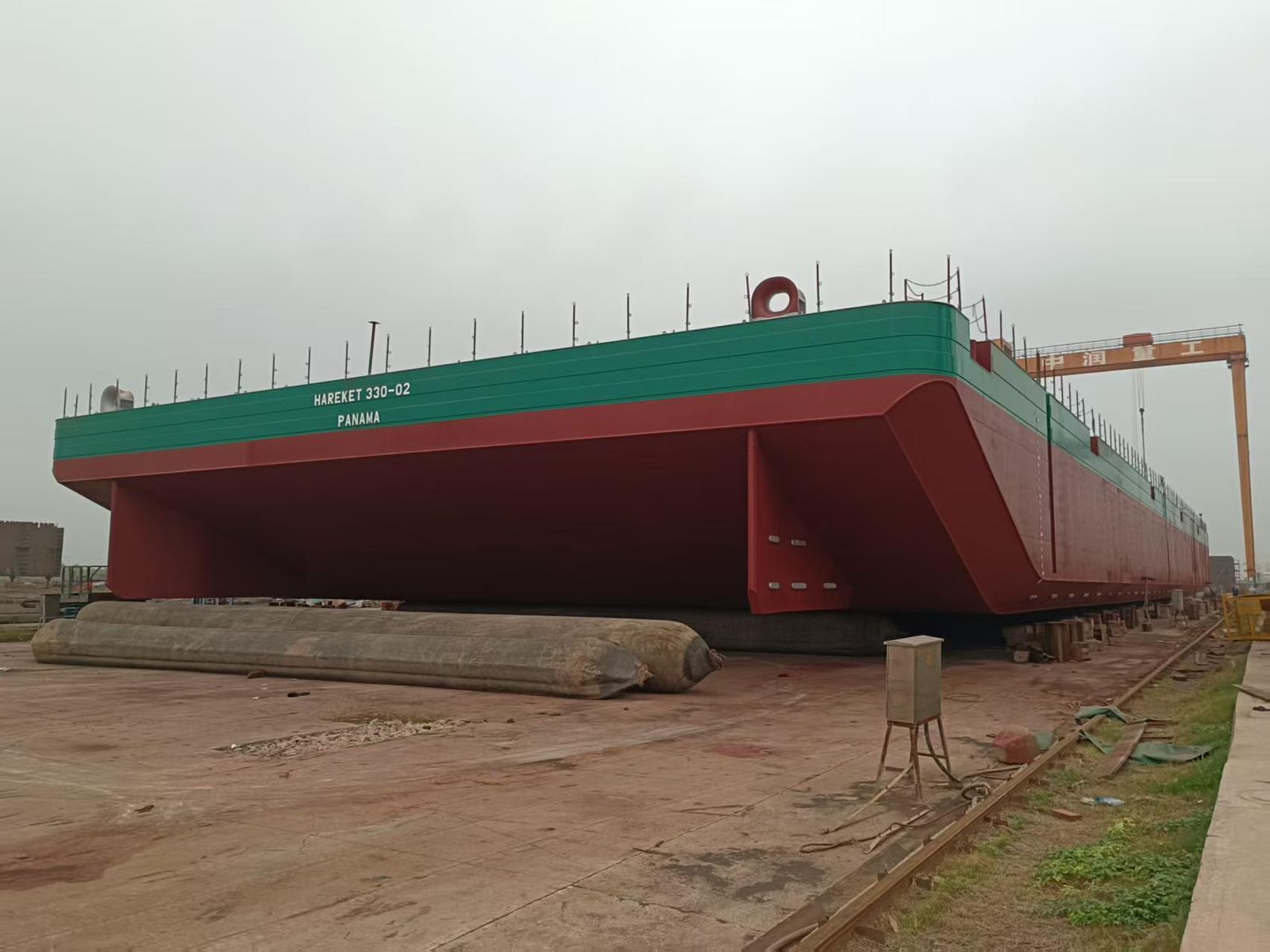 A large red and green barge, labeled "HAREKET 330-02 PANAMA," supported by airbags on land.