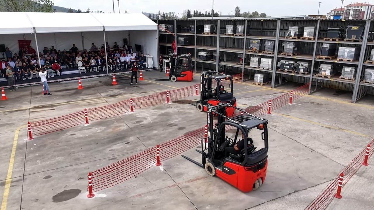 Two red forklifts on an obstacle course, with an audience and storage racks in the background.