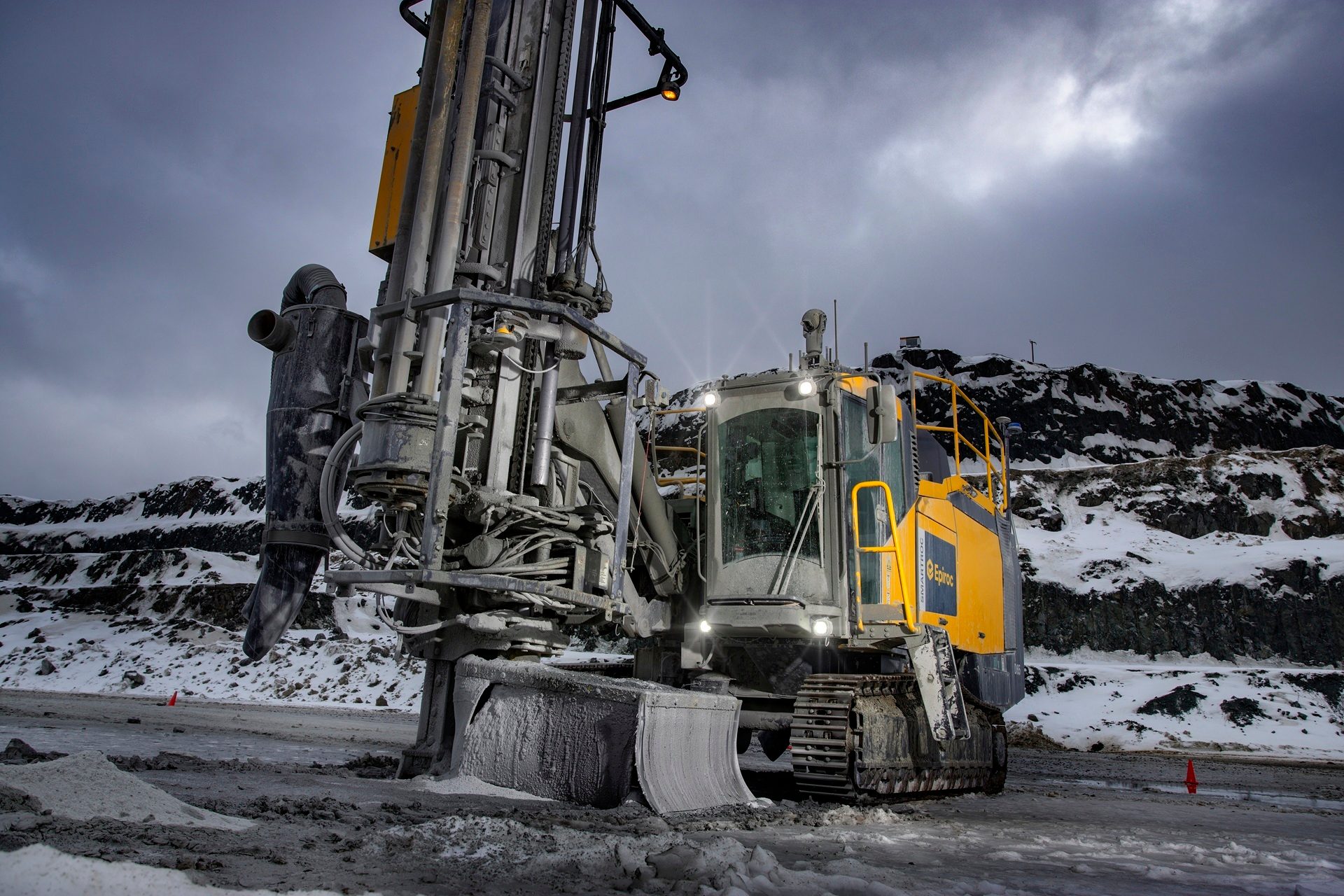 Heavy-duty drilling rig in a snowy mine, cloudy sky.