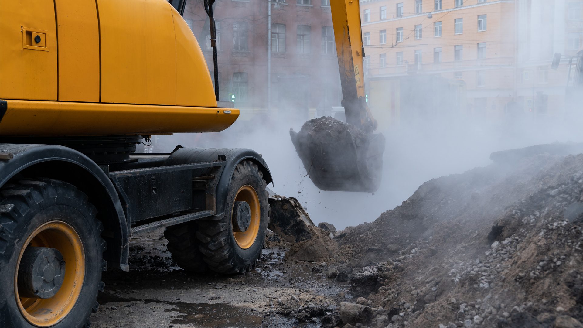 Excavator digging dirt amidst heavy steam in an urban street.