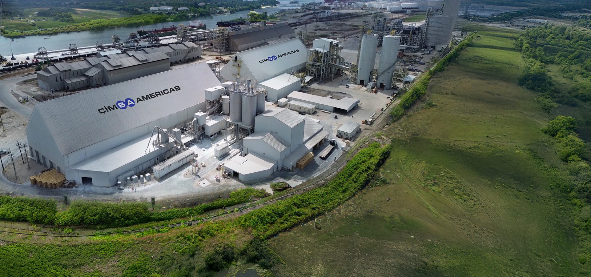 Aerial view of the CIMSA AMERICAS industrial facility by a river, with multiple buildings and silos.