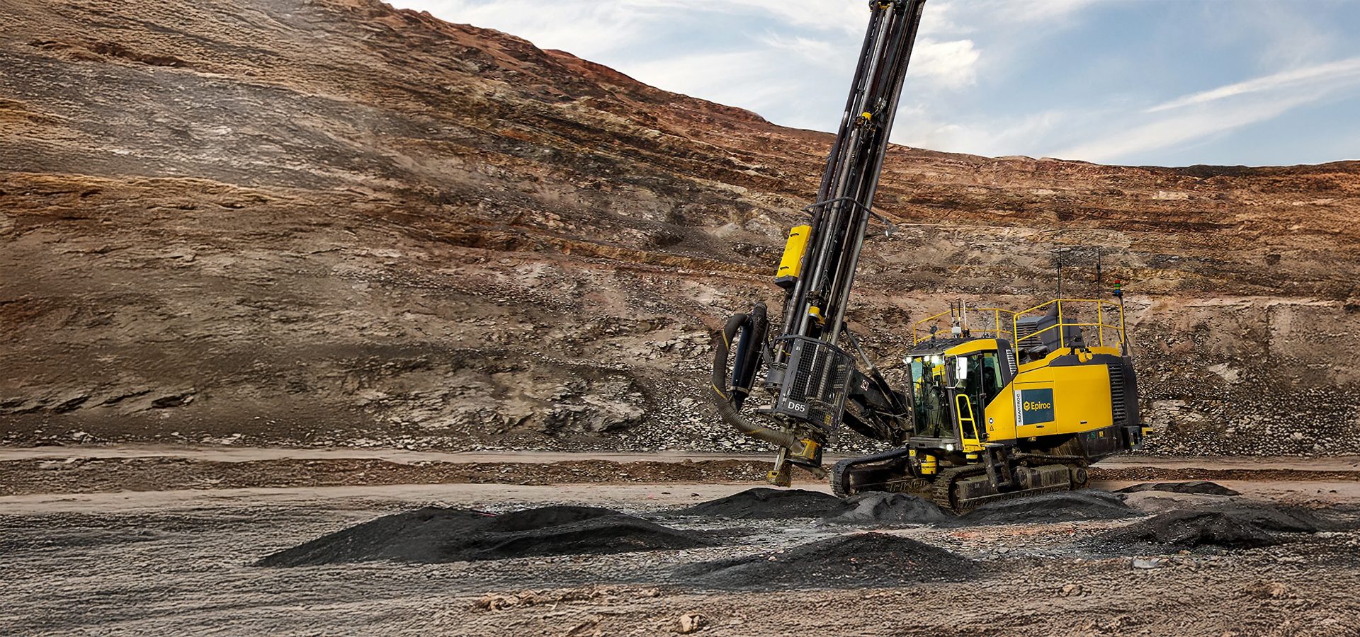 Epiroc D65 drilling rig in an open-pit mine, surrounded by layered rock formations.