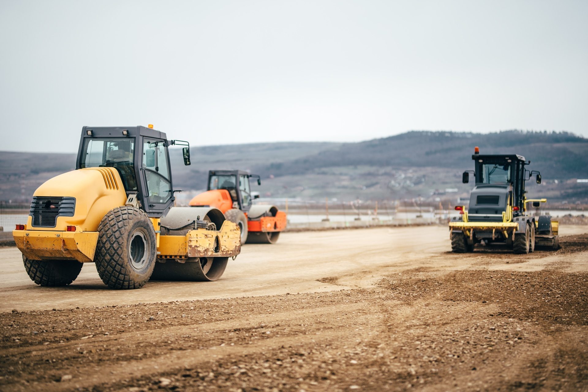Three road rollers on a dirt road at a construction site.