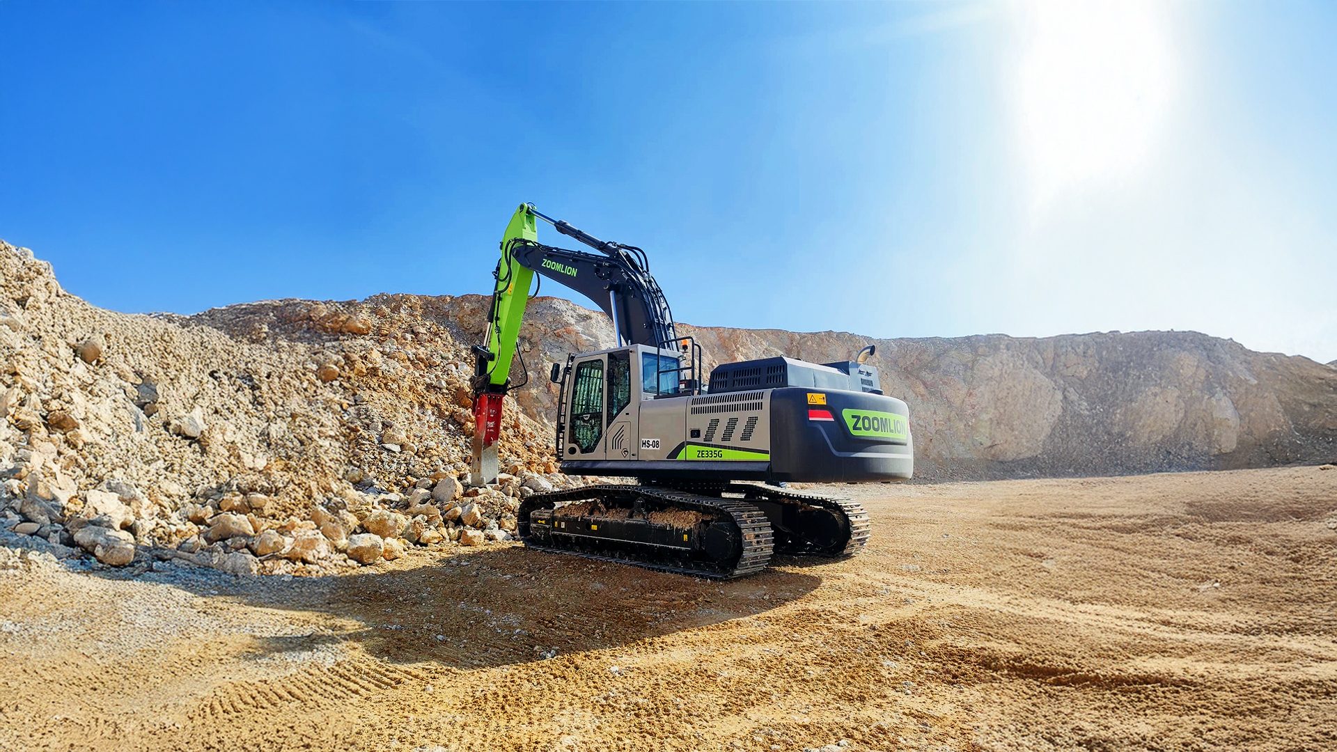 A Zoomlion excavator with a hydraulic hammer attachment sits in a sunny quarry, surrounded by rock piles.