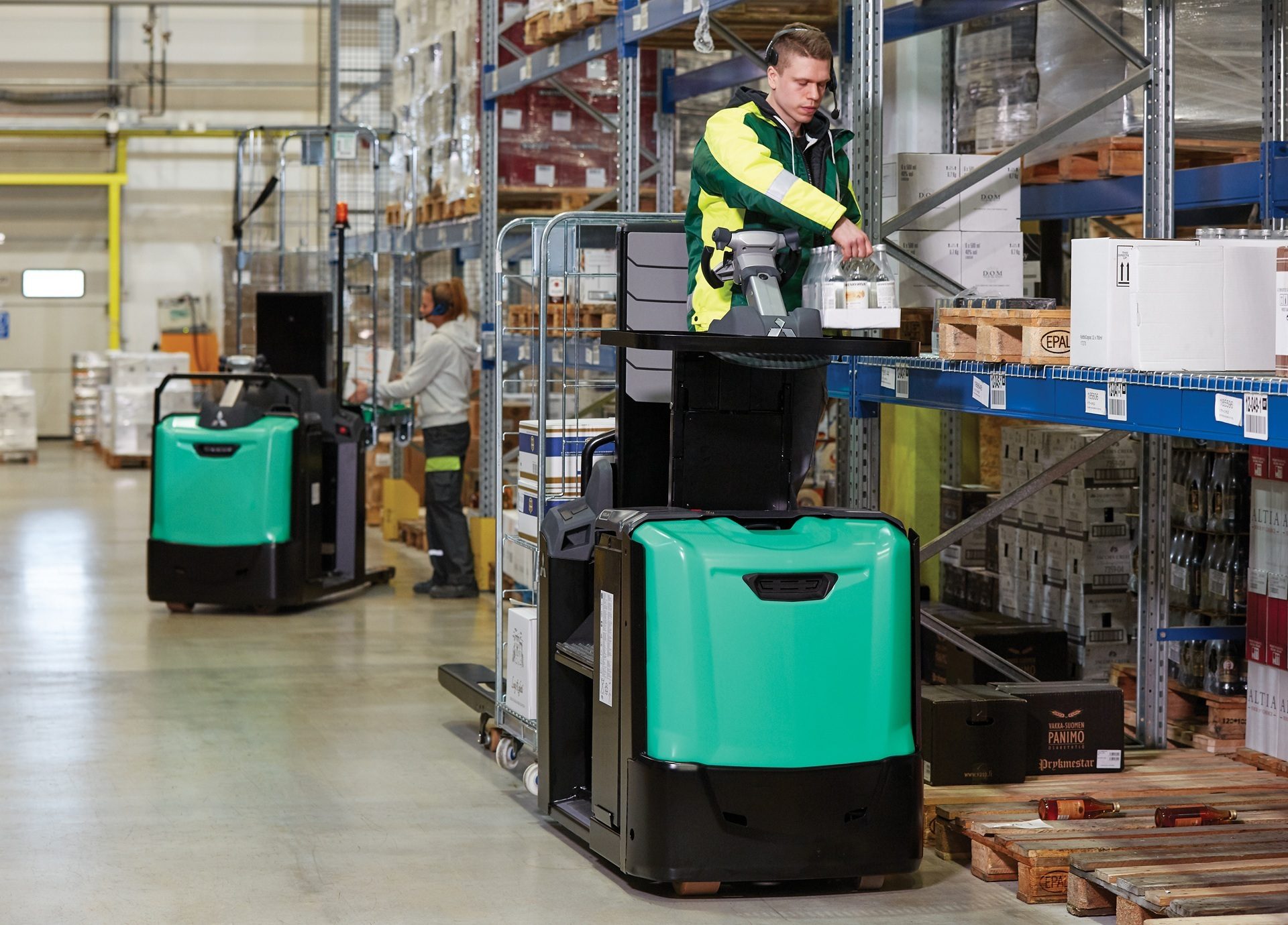 Warehouse workers using electric order pickers to fulfill orders from shelves in a large logistics facility.