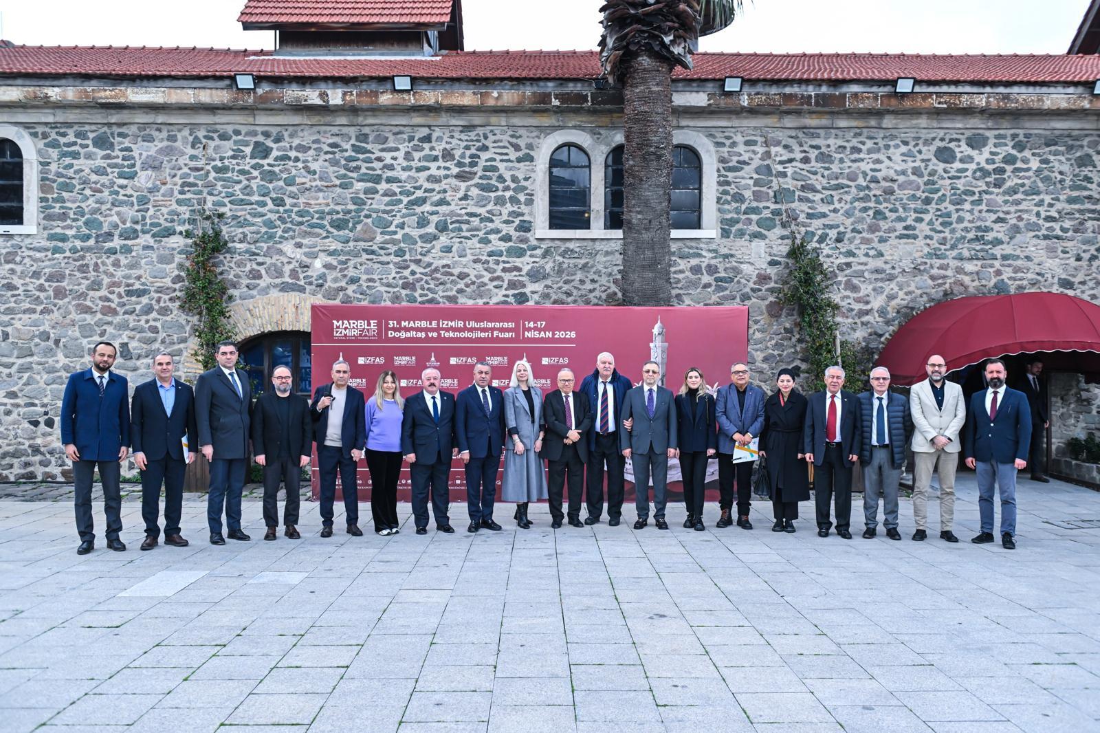 A group of professionals, including men and women, stand in front of a red banner for the Marble İzmir Fair.