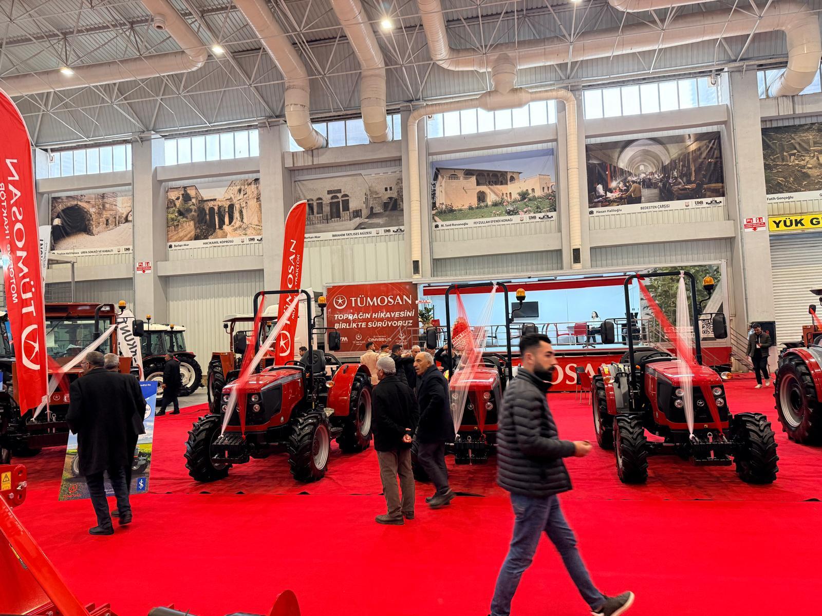 Indoor exhibition featuring red tractors on a red carpet, with attendees and historical photo banners.