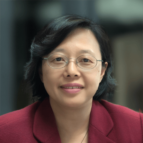 A smiling East Asian woman with dark hair and round glasses in a red blazer.