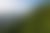 A gondola travels over a vast evergreen forest on a mountain, with a lake and distant peaks under a bright sky.