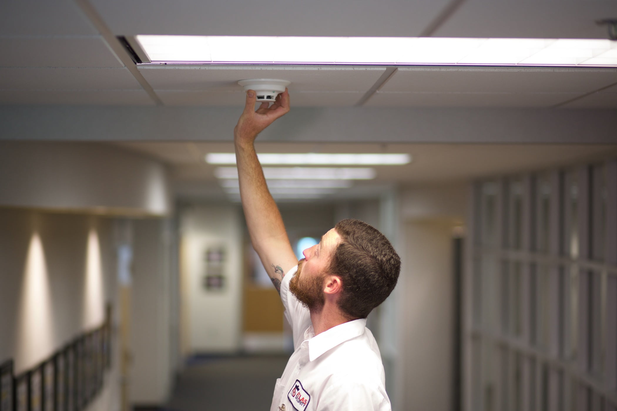 A fire technician replaces a typical smoke detector in a nursing home hallway. 